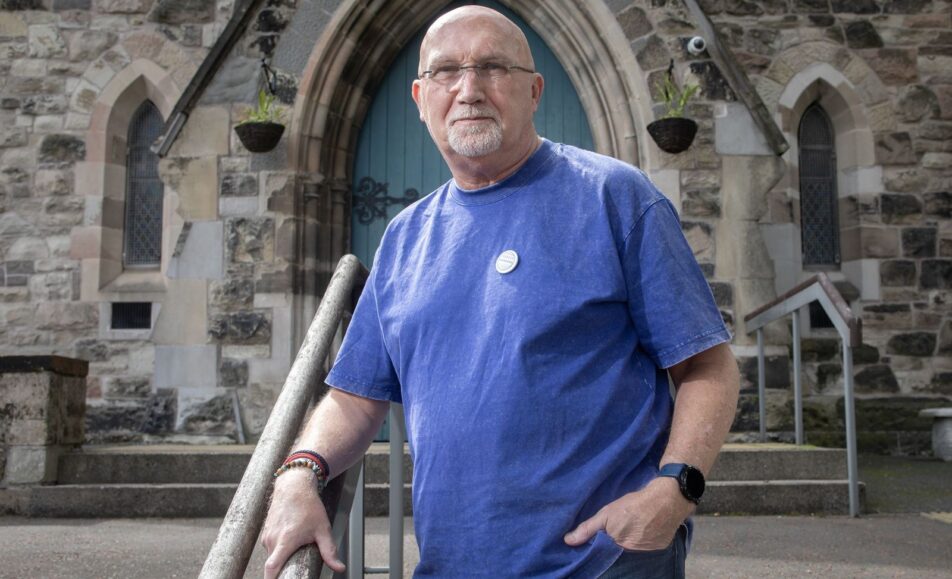 Rev Bill Shaw standing by a handrail outside a stone church with a blue arched door